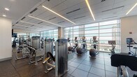 Located at 340 E North Water St in Chicago's Streeterville neighborhood, this fitness center offers a comprehensive, multi-zone workout facility with striking views of the city skyline and Lake Michigan. The main exercise floor is lined with floor-to-ceiling windows that flood the space with natural light while framing panoramic views of the surrounding cityscape. This area is outfitted with a full suite of Precor strength machines, treadmills, ellipticals, and free weights, all set on durable rubber flooring designed for high-performance use. Linear LED lighting runs across the ceiling, providing consistent illumination throughout. A dedicated functional training zone features a heavy bag, TRX suspension systems, kettlebells, and a rowing machine, positioned alongside expansive windows that maintain the open, light-filled atmosphere. A mirrored studio area accommodates spin bikes and group fitness activities, enhanced by large wall mirrors that amplify the sense of space. Additional areas include a stretching and floor exercise zone with carpeted flooring, a flat-screen display, and full-wall mirrors. The facility also includes a check-in area with a reception counter and glass entry doors. Throughout, the design balances modern aesthetics with functional versatility, creating an energizing environment for a wide range of fitness pursuits.