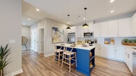 Located at 1500 Westshore Dr in Cumming, Georgia, this single-floor residence offers a thoughtfully designed layout with modern finishes throughout. The open-concept kitchen serves as a focal point, showcasing crisp white shaker cabinetry with brushed gold hardware, a classic subway tile backsplash, stainless steel appliances, and a striking cobalt blue island with a white quartz countertop and built-in open shelving. Pendant lighting overhead adds a contemporary touch, while warm wood-look flooring flows seamlessly throughout the main living areas. The living room is bright and welcoming, with large windows that invite natural light and a ceiling fan overhead. Bedrooms feature plush carpeting, generous closet space including walk-in options, and large windows that enhance the airy, light-filled atmosphere. The primary bathroom continues the bold blue design theme with navy shaker-style cabinetry, a framed vanity mirror, and wood-look flooring that ties the space together. A secondary kitchen or utility area features white cabinetry, quartz countertops, a gold-toned faucet, and a stainless steel dishwasher, adding exceptional functionality. The overall design balances clean, neutral tones with carefully selected accent details, creating a cohesive and inviting living environment.