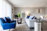 This single-floor residence offers a thoughtfully designed layout that balances functionality and comfort across its key living spaces. The open-concept living and dining area serves as the heart of the home, featuring warm wood-look flooring, neutral gray walls, and a textured ceiling throughout. A ceiling fan keeps the space comfortable, while a large sliding glass door dressed with vertical blinds floods the living room with natural light and opens to a private outdoor patio. The galley-style kitchen is well-equipped, showcasing white shaker cabinetry, dark countertops, black stainless appliances including a refrigerator and electric range, and a window above the sink for added brightness. The residence includes multiple bedrooms, each finished with the same wood-look flooring, neutral tones, and textured ceilings. Bedrooms benefit from natural light via windows with sheer curtains, and closet space is provided in each room. One bedroom features a standard reach-in closet, while a hallway area leads to a generous open shelving storage closet, ideal for linens or additional organization. The overall ambiance is clean, modern, and inviting, with a cohesive neutral palette that lends itself well to a variety of interior styles.