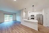 Located at 1061 Dryden Rd in Ithaca, NY, this well-designed two-bedroom, three-bathroom home spans two floors and offers a clean, modern aesthetic throughout. The main living floor hosts the primary living spaces, including a bright, open-concept area that seamlessly integrates the kitchen, dining, and living room. The kitchen is a standout feature, outfitted with crisp white shaker cabinets, a white quartz peninsula with a black undermount sink, stainless steel appliances, and stylish pendant lighting. Warm wood-look flooring flows throughout this level, complementing the light-filled interior. A sliding glass door connects the living area to an outdoor balcony, bringing in natural light and neighborhood views. The two bedrooms are comfortably sized and carpeted, with large windows overlooking the surrounding community. Ample closet space is distributed throughout the home, with five closets total. A dedicated in-unit laundry room houses a stacked washer and dryer. Three full bathrooms provide convenience for residents and guests alike. The lower level includes an attached garage, offering secure parking and additional storage. The home's clean lines, contemporary finishes, and functional layout make it a practical and attractive residence in the Ithaca area.