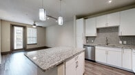Located at 14900 Memorial Dr in Houston, TX, this well-appointed one-bedroom, one-bathroom residence offers a thoughtfully designed single-level layout. The open-concept kitchen and living area serves as the heart of the home, featuring white cabinetry that extends to the ceiling, a mosaic tile backsplash, stainless steel appliances including a refrigerator, range, microwave, and dishwasher, and a granite-topped center island illuminated by modern pendant lighting. Track lighting and a ceiling fan complete the functional yet stylish kitchen space. Rich hardwood-style flooring flows throughout the main living areas, adding warmth and continuity. The living room is bright and spacious, with access to a private balcony through a glass door framed by a window, inviting natural light throughout the day. The bedroom is carpeted for comfort and features a ceiling fan and a large window with blinds. Three closets provide generous storage, including a walk-in closet with multi-level hanging rods and shelving. The bathroom offers a granite-topped vanity, a soaking tub, and a tiled shower surround in a warm stone finish. An in-unit laundry area adds everyday convenience, rounding out this efficiently designed and modern Houston residence.