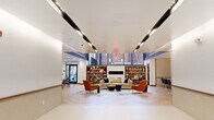 Located at 27 Park Rd in West Hartford, CT, this thoughtfully designed single-floor space combines contemporary aesthetics with functional versatility. The layout flows seamlessly across several distinct zones, all unified by herringbone-patterned hardwood flooring and a cohesive modern palette.

The main lounge area serves as the heart of the space, featuring soaring double-height ceilings accented by bold navy blue architectural elements and a striking sculptural chandelier. Comfortable seating arrangements—including plush sofas, accent chairs in warm terracotta tones, and coffee tables—are anchored by a large abstract area rug, creating an inviting and social atmosphere. Built-in bookshelves flank a central fireplace, adding warmth and character.

The entry corridor features sleek recessed linear lighting and glass-paneled doors, leading naturally into the open lounge. A designated dining nook with tufted leather banquette seating and marble-top tables provides an intimate setting for gatherings.

A private meeting room offers a refined environment with warm wood paneling, a marble conference table, and a large wall-mounted display screen. The kitchen area is a standout feature, showcasing navy cabinetry, a generous marble-topped island with wood bar stools, pendant lighting, and gold-toned ceiling details, delivering both style and practicality.