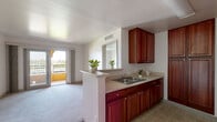 Located in the Eagle Rock neighborhood of Los Angeles, this one-bedroom, one-bathroom residence offers a thoughtfully organized single-floor layout. The galley-style kitchen is a standout feature, outfitted with rich, dark wood cabinetry providing generous storage, light countertops, black appliances including an electric range and built-in microwave, and tile flooring. A peninsula counter with a sink opens toward the dining and living areas, creating a cohesive flow throughout the main living space. The combined dining and living room is bright and inviting, with carpeted flooring and a sliding glass door that leads directly to a private balcony with open views of the surrounding Los Angeles streetscape and greenery. The spacious bedroom offers comfortable proportions, plush carpet, and access to a well-sized closet with built-in shelving. The bathroom is clean and functional, featuring a wood vanity with a large mirror, a tub-shower combination, and tile flooring. Throughout the residence, neutral tones and consistent cabinetry finishes create a cohesive, understated aesthetic well suited to city living.