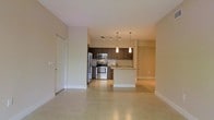 This single-floor space showcases a thoughtfully designed open-concept layout that seamlessly connects the living area to the kitchen, creating a bright and functional environment. Light-toned tile flooring extends throughout, lending a clean and cohesive aesthetic to the entire space.

The kitchen is a standout feature, outfitted with rich dark cabinetry that provides ample storage and a striking contrast against the neutral surroundings. A classic subway tile backsplash adds texture and visual interest, while granite countertops offer both durability and style. A central kitchen island serves as a natural gathering point and adds additional counter space. Stainless steel appliances — including a refrigerator, electric range, and built-in microwave — complete the modern kitchen ensemble.

Overhead, a combination of track lighting and elegant pendant lights illuminates the kitchen area, enhancing both task lighting and ambiance. The open living area benefits from the natural flow of the layout, offering a versatile space for a variety of furnishing arrangements. A closet near the entryway provides convenient storage. The overall ambiance is contemporary and inviting, characterized by neutral tones, clean lines, and a well-balanced blend of form and function.