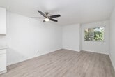 This single-floor, 2-bedroom, 1-bathroom unit offers a clean, modern aesthetic unified by light wood-style vinyl flooring and crisp white walls throughout. The living area is bright and open, featuring a ceiling fan with integrated lighting and a window that frames outdoor greenery, creating a fresh, airy atmosphere.

The spacious primary bedroom continues the consistent flooring and neutral palette, with a ceiling fan, white blinds, and a window overlooking lush vegetation, allowing ample natural light. The second bedroom is similarly finished, with white walls, matching flooring, and a well-positioned window that brightens the space.

The kitchen has been thoughtfully updated with white shaker-style cabinetry, white quartz countertops, and a full suite of stainless steel appliances, including an electric range, built-in microwave, and dishwasher. A window above the sink brings in additional natural light, enhancing the clean, functional design.

The bathroom features a white vanity with a quartz countertop, brushed nickel fixtures, a framed mirror, and a small window for ventilation. The overall design of this unit is cohesive and contemporary, prioritizing clean lines and a bright, neutral palette.