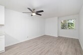 This single-floor, 2-bedroom, 1-bathroom unit offers a clean, modern aesthetic unified by light wood-style vinyl flooring and crisp white walls throughout. The living area is bright and open, featuring a ceiling fan with integrated lighting and a window that frames outdoor greenery, creating a fresh, airy atmosphere.

The spacious primary bedroom continues the consistent flooring and neutral palette, with a ceiling fan, white blinds, and a window overlooking lush vegetation, allowing ample natural light. The second bedroom is similarly finished, with white walls, matching flooring, and a well-positioned window that brightens the space.

The kitchen has been thoughtfully updated with white shaker-style cabinetry, white quartz countertops, and a full suite of stainless steel appliances, including an electric range, built-in microwave, and dishwasher. A window above the sink brings in additional natural light, enhancing the clean, functional design.

The bathroom features a white vanity with a quartz countertop, brushed nickel fixtures, a framed mirror, and a small window for ventilation. The overall design of this unit is cohesive and contemporary, prioritizing clean lines and a bright, neutral palette.