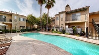Located at 40800 Sunflower Road in Murrieta, California, this inviting outdoor amenity space showcases a distinctive Spanish Colonial architectural style, characterized by warm stucco exteriors, terracotta tile rooflines, arched design accents, and decorative diamond-pattern facade detailing. At the heart of the space is a generously sized freeform swimming pool with crystal-clear turquoise water, complete with a built-in fountain feature that adds a dynamic visual element. The pool is surrounded by an expansive stamped concrete deck, providing ample room for lounging and recreation. Poolside amenities include multiple chaise lounge chairs and shaded dining areas with umbrella-covered tables, ideal for relaxing in the Southern California sun. Towering palm trees are strategically placed throughout the courtyard, lending a tropical, resort-like atmosphere while providing natural shade. The pool area is enclosed by a wrought-iron security fence, ensuring a safe and well-defined environment. Adjacent multi-story residential buildings with private balconies frame the courtyard on multiple sides, creating an intimate and sheltered setting. The overall ambiance is one of a well-appointed, resort-inspired retreat designed for outdoor leisure and community gathering.