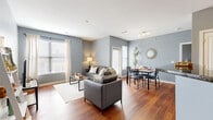 This thoughtfully designed 2-bedroom, 2-bathroom residence offers a functional and cohesive single-floor layout. The open-concept living, dining, and kitchen area forms the heart of the home, bathed in natural light from multiple windows dressed with classic blinds and flowing curtains. Rich hardwood flooring runs throughout the main living spaces, complementing the cool blue-gray walls that lend a calm, modern aesthetic.

The living room provides a comfortable gathering space, while the adjacent dining area accommodates a full dining table for four. The kitchen is well-equipped with warm honey-toned wood cabinetry, dark granite countertops, stainless steel appliances including a refrigerator, range, and microwave, and a double sink — offering both style and practicality.

The primary bedroom features plush carpeting and direct access to an en-suite bathroom with a glass-enclosed shower and tile surround. The second bedroom is generously sized with carpeted flooring, a bright window, and easy access to the second full bathroom, which includes a tiled tub-shower combination. Two closets provide ample storage throughout the unit. A welcoming entry corridor connects all areas seamlessly, making this a well-organized and comfortable living space.