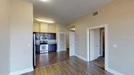 This single-floor 1-bedroom, 1-bathroom unit offers a functional and cohesive layout designed for comfortable everyday living. The open-concept living and dining area is finished with rich hardwood-style flooring and features a ceiling fan with light fixture, creating a bright and airy atmosphere. Natural light streams in through large windows dressed with blinds, adding warmth to the neutral-toned walls throughout.

The kitchen is positioned adjacent to the living area and is outfitted with dark espresso cabinetry, stainless steel appliances including a refrigerator, electric range, and built-in microwave, all set atop durable tile flooring. A louvered closet door provides additional storage nearby.

The bedroom is a comfortable retreat with plush carpet flooring, a ceiling fan, and a window overlooking the outdoors. It connects to a generous walk-in closet equipped with wire shelving and hanging rods, offering ample storage capacity.

The bathroom continues the dark cabinetry theme with a single-sink vanity topped with a white countertop, complementary mirror, and elegant overhead lighting. Tile flooring ties the space together cohesively. A hallway connects the rooms, completing this well-organized and move-in-ready layout.