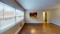Located at 3566 Minikahda Ct in St. Louis Park, Minnesota, this single-floor residence offers a clean, functional layout designed for comfortable everyday living. The main living area is finished with warm hardwood flooring that extends throughout, neutral-toned walls, and white baseboard trim that gives the space a bright, cohesive feel. A large window in the living area invites abundant natural light and provides pleasant outdoor views of the surrounding greenery. Baseboard heating units are positioned along the exterior walls, ensuring efficient warmth throughout the colder Minnesota months. A standout architectural detail is the pass-through window connecting the living and dining area to the kitchen, which features dark cabinetry and a tile backsplash, creating a convenient and open sightline between spaces. A dedicated bedroom area is outfitted with a ceiling fan and light fixture, adding both comfort and functionality. The full bathroom includes tile flooring in warm earth tones, a vanity with wood cabinetry, a toilet, and a full tub and shower combination enclosed by classic white subway tile and a chrome curtain rod. The overall ambiance of this unit is practical and well-maintained, offering a straightforward residential experience in a quiet St. Louis Park location.
