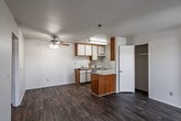 Located at 16850 Jasmine St in Victorville, California, this single-floor unit offers a functional and straightforward layout designed for comfortable everyday living. The open living and dining area is finished with durable wood-look flooring that runs throughout the space, lending a cohesive and clean aesthetic. A ceiling fan with light fixture keeps the area well-ventilated, while white walls and a textured ceiling contribute to a bright, neutral atmosphere. A peninsula-style kitchen counter with warm wood cabinetry serves as a natural divider between the living space and the galley kitchen. The galley kitchen itself is efficiently arranged with white upper and lower cabinets, a light-toned countertop, a freestanding electric range, and a full-size refrigerator, providing ample storage and prep space. The bedroom is a well-proportioned room featuring a large window with vertical blinds that allows natural light to fill the space, along with a wall-unit air conditioner and a dedicated closet for storage. The bathroom is equipped with a single-sink vanity with a quartz-style countertop, a full tub-shower combination with grab bars for accessibility, and consistent wood-look flooring. The overall design is clean and practical, making this a functional space suited for a variety of occupants.