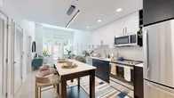 This thoughtfully designed one-bedroom, one-bathroom residence offers a smart and efficient layout spread across a single floor. The open-concept kitchen and living area serves as the heart of the home, where a sleek, modern kitchen commands attention with two-tone cabinetry — crisp white uppers paired with deep charcoal lowers — accented by a herringbone tile backsplash and a full suite of stainless steel appliances. Light wood flooring runs throughout, creating a warm, cohesive feel. A central island with bar seating adds both functionality and style, ideal for casual dining or entertaining. The living area benefits from floor-to-ceiling windows and glass doors that open to a private outdoor balcony, flooding the space with natural light and lush greenery views. The bedroom continues the bright, airy aesthetic with tall windows overlooking the outdoors and ample room for a full furniture arrangement, complemented by a dedicated closet. The bathroom features a clean, minimalist design with white subway tile, a shower-tub combination, and a streamlined vanity. Recessed lighting and a modern linear pendant in the kitchen complete the polished, contemporary character of this well-appointed residence.