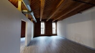 Located on the historic Washington Avenue corridor in downtown St. Louis, this 2-bedroom, 1-bathroom loft blends industrial character with modern comfort. The space is defined by its striking exposed wood beam ceilings with tongue-and-groove planking, original brick accent walls, and durable wood-look plank flooring that runs throughout. Oversized windows flood the living area with natural light while offering views of the surrounding urban streetscape.

The open-plan kitchen and dining area features light maple cabinetry, granite-look countertops, stainless steel appliances including a dishwasher and range, and a peninsula breakfast bar — all set beneath pendant lighting and those signature timber beams. Exposed ductwork reinforces the loft's industrial aesthetic.

The generously sized primary bedroom includes closet access and maintains the same warm ceiling treatment, creating a cohesive feel. The second bedroom offers similar proportions with its own closet. The bathroom is clean and functional, appointed with white subway tile surrounding a full soaking tub and shower combination, complemented by matte black fixtures and hardware. Two additional closets provide ample storage throughout the unit. The overall ambiance is urban and characterful, ideal for those who appreciate architectural history paired with updated living spaces.