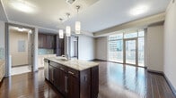 This well-appointed 2-bedroom, 3-bathroom residence offers a thoughtfully designed single-floor layout with a refined urban aesthetic. The open-concept living and kitchen area serves as the heart of the home, anchored by a large center island with striking granite countertops and a double sink, complemented by dark espresso cabinetry, mosaic tile backsplash, stainless steel appliances, and elegant pendant lighting. Rich hardwood flooring flows throughout the main living areas, reflecting abundant natural light that pours in through expansive floor-to-ceiling windows and glass balcony doors, framing sweeping city skyline views.

The spacious living area transitions seamlessly from the kitchen, offering an airy, open feel with tray ceiling detailing. A long hallway with track lighting connects the bedrooms and bathrooms, providing a clear division between living and sleeping areas. Both bedrooms feature plush carpeting and tray ceilings; the primary suite includes a dedicated walk-in closet, while the secondary bedroom enjoys generous city views through a large picture window. The bathrooms are finished with tile flooring, and the closets are equipped with built-in wire shelving systems. A dedicated laundry room with a full-size washer and dryer adds everyday convenience, completing this polished urban residence.
