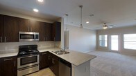 This 2-bedroom, 2-bathroom residence features the B3 floor plan, delivering a well-appointed single-story layout designed for comfortable, modern living. The open-concept kitchen is a standout centerpiece, showcasing rich dark-espresso cabinetry, light granite countertops, and a peninsula island with a double undermount sink — ideal for both meal prep and casual dining. Stainless steel appliances, including an electric range and built-in microwave, add a sleek, contemporary touch. Pendant lighting above the island and recessed ceiling lights throughout ensure a bright, well-lit environment. The kitchen flows seamlessly into the living area, which features plush carpeting, a ceiling fan, and a window that invites natural light into the space, creating a warm and inviting ambiance. Light hardwood-style flooring in the kitchen transitions naturally into the carpeted living space, adding visual contrast and definition between the two areas. Crown molding details along the ceiling lend a refined architectural touch. With two full bathrooms and two generously sized bedrooms, this floor plan offers a functional and comfortable layout suited for a variety of lifestyles.