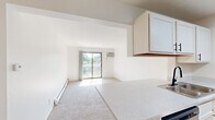 Located at 5220 Kellogg Woods Dr SE in Kentwood, Michigan, this one-bedroom residence offers a practical and comfortable single-floor layout designed for efficient everyday living. The combined kitchen and living area forms the heart of the home, where light-toned luxury vinyl plank flooring runs throughout the kitchen, creating a clean and modern feel. The galley-style kitchen is well-equipped with white cabinetry featuring black hardware, light stone countertops, a double-basin sink with a matte black faucet, a dishwasher, electric range, over-the-range microwave, and a stainless steel refrigerator. A pass-through window connects the kitchen to the carpeted living room, enhancing the open feel of the shared space. The living room benefits from natural light and direct access to a private balcony through a sliding glass door, offering pleasant outdoor views of surrounding greenery. The bedroom is a well-sized retreat finished with plush carpeting, a baseboard heating unit, and a double-door closet providing ample storage. Clean white walls and consistent trim work throughout give the space a bright, neutral aesthetic that is easy to personalize. Baseboard heating is present in both the living room and bedroom, ensuring year-round comfort.