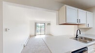 Located at 5220 Kellogg Woods Dr SE in Kentwood, Michigan, this one-bedroom residence offers a practical and comfortable single-floor layout designed for efficient everyday living. The combined kitchen and living area forms the heart of the home, where light-toned luxury vinyl plank flooring runs throughout the kitchen, creating a clean and modern feel. The galley-style kitchen is well-equipped with white cabinetry featuring black hardware, light stone countertops, a double-basin sink with a matte black faucet, a dishwasher, electric range, over-the-range microwave, and a stainless steel refrigerator. A pass-through window connects the kitchen to the carpeted living room, enhancing the open feel of the shared space. The living room benefits from natural light and direct access to a private balcony through a sliding glass door, offering pleasant outdoor views of surrounding greenery. The bedroom is a well-sized retreat finished with plush carpeting, a baseboard heating unit, and a double-door closet providing ample storage. Clean white walls and consistent trim work throughout give the space a bright, neutral aesthetic that is easy to personalize. Baseboard heating is present in both the living room and bedroom, ensuring year-round comfort.