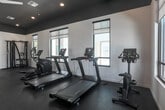 Located at 18730 Miner Ln in Morgan Hill, CA, this well-appointed fitness center offers a clean, modern environment designed to support a complete workout routine. The single-floor exercise room is laid out with an open, spacious feel, making it easy to move between equipment and exercise areas without feeling crowded.

The room features a contemporary design with a bold dark ceiling contrasted against crisp white walls, creating a sleek, focused atmosphere. Recessed lighting and a ceiling fan ensure the space remains well-lit and comfortable during workouts. Large, multi-pane windows line the walls, flooding the room with natural light and providing views of the surrounding outdoor environment.

The exercise room is equipped with multiple treadmills, an elliptical trainer, a stationary bike, and a multi-function cable/strength machine, offering a well-rounded selection of cardio and resistance training options. The flooring consists of durable, dark rubber tiles that provide cushioning and stability during exercise. A full-width wall mirror spans one side of the room, visually expanding the space and allowing users to monitor their form. The open floor area in front of the mirror provides additional room for stretching, bodyweight exercises, or free-form movement. The overall ambiance is modern, clean, and functional, making this fitness center a practical and inviting space for daily exercise.