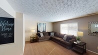 This single-floor residence offers a thoughtfully arranged layout that maximizes comfort and functionality throughout. The living room serves as the central gathering space, featuring warm carpeted flooring, a textured patterned ceiling, and a large window fitted with blinds that invites natural light while maintaining privacy. A neutral two-tone color scheme on the walls adds depth and character to the room.

Adjacent to the living area, the dining room provides an intimate setting accented by a stylish globe pendant light and a chalkboard accent wall that adds a creative touch. A pass-through connects seamlessly to the galley-style kitchen, which is equipped with warm wood cabinetry, granite-look countertops, a double-basin sink, and white appliances including a refrigerator and range.

The bedroom is generously sized with plush carpeting, a decorative textured ceiling, and a bright window that fills the space with natural light. A walk-in closet offers substantial storage, keeping the room organized and clutter-free.

The bathroom features warm-toned tile flooring, a wood-cabinet vanity with a mirrored medicine cabinet, and overhead vanity lighting. Throughout the residence, consistent textured ceilings and neutral wall tones create a cohesive and inviting atmosphere.