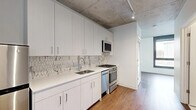 Located at 918 West School Street in Chicago's vibrant Lakeview neighborhood, this efficiently designed single-floor unit offers a thoughtfully laid-out living space with a clean, contemporary aesthetic. The interior is defined by striking exposed concrete ceilings that lend an industrial character, complemented by warm hardwood flooring that runs throughout the main living areas.

The kitchen is a standout feature, outfitted with crisp white cabinetry extending floor to ceiling, a decorative hexagonal marble-patterned tile backsplash, quartz countertops, a stainless steel sink, and a full suite of stainless steel appliances including a gas range, dishwasher, over-the-range microwave, and refrigerator. Track lighting above adds both function and style.

The bathroom continues the modern, clean theme with large-format marble-look porcelain floor tiles, a white vanity with under-sink storage, a wall-mounted mirror, and a tiled shower-tub combination. The space also includes two closets for ample storage and a dedicated laundry area for added convenience.

The main living area benefits from a large floor-to-ceiling window that frames views of the surrounding Chicago streetscape, filling the room with natural light. The unit's efficient layout and refined finishes make it a polished urban retreat.