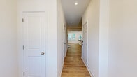 This two-story home offers a well-organized layout across two floors, with the main living areas on the ground floor and bedrooms situated above. The lower level houses an open-concept kitchen and living room, an entrance, and an attached garage. The kitchen is a standout feature, equipped with gray shaker-style cabinetry, stainless steel appliances including a refrigerator, range, and microwave, a white quartz island with an integrated sink and seating overhang, and a white subway tile backsplash. Light hardwood-style flooring runs throughout the main level, complementing the bright, neutral color palette and recessed lighting overhead. Natural light flows in through multiple windows facing the living area.

The upper floor hosts all three bedrooms and two full bathrooms. Bedrooms are finished with plush carpet and feature windows with blinds. The generously sized primary bedroom connects to a private en-suite bathroom showcasing large-format tile flooring and a glass-enclosed walk-in shower with a built-in bench. A dedicated walk-in closet with wire shelving provides ample storage. The remaining bedrooms share access to a second bathroom. The garage includes an automatic door opener and an electrical panel.