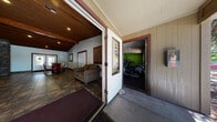 This single-story community clubhouse is thoughtfully designed to serve as a central hub for social and wellness activities. The layout encompasses several distinct functional zones, each with its own character and purpose.

The lounge area is a welcoming space defined by a rich wood-paneled ceiling with exposed beams and recessed lighting, creating a warm, intimate ambiance. Multiple sofas arranged around a decorative glass-top coffee table rest on a vibrant, patterned area rug, while large windows allow natural light to fill the room. An adjacent dining area features a glass-top table surrounded by tufted leather chairs, with double glass doors that open to the outdoors.

The kitchen is well-appointed with warm wood cabinetry, stone-look tile flooring, and a full suite of stainless steel appliances, including a refrigerator, range, microwave, and dishwasher, making it well-suited for community events.

The fitness center is a standout feature, divided into two connected areas. One zone is energized by bold green accent walls, wall-mounted mirrors, a mounted television, and a variety of cardio machines including ellipticals, stair climbers, and stationary bikes. The adjoining strength-training area offers multiple cable machines, free weights, and weight benches set on protective rubber flooring.