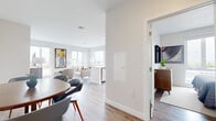 This well-appointed 2-bedroom, 2-bathroom unit at 50 Salt St in Revere, MA offers a thoughtfully designed open-concept layout with modern finishes throughout. Light wood-tone flooring flows seamlessly through the living, dining, and kitchen areas, creating a cohesive and airy atmosphere. The living room is bright and welcoming, anchored by large windows that frame scenic outdoor views and fill the space with natural light. The kitchen is sleek and functional, featuring warm wood cabinetry, a bold navy tile backsplash, stainless steel appliances, and a white quartz peninsula that doubles as a casual dining surface. Both bathrooms are finished with marble-look tile flooring, warm wood vanities, white quartz countertops, and large mirrors, lending a clean, spa-like aesthetic. The primary bedroom enjoys generous proportions and a large window with expansive views, while the second bedroom offers a similarly serene, minimalist design with light wood flooring. Crisp white walls throughout the unit enhance the sense of openness and complement the contemporary design palette. The overall ambiance is modern, clean, and comfortable, making this a refined and practical residence in Revere.