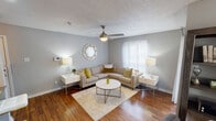 This single-floor unit is thoughtfully designed with a cohesive gray and neutral color palette that creates a calm, modern atmosphere throughout. Rich wood-look flooring flows continuously across all rooms, adding warmth and visual continuity to the space.

The living area serves as the heart of the unit, featuring a ceiling fan with integrated lighting and multiple windows dressed with sheer curtains and blinds that invite natural light. A sliding glass door opens to an outdoor patio, providing a seamless indoor-outdoor connection. The room comfortably accommodates a large sectional sofa arrangement centered around a round coffee table.

The galley-style kitchen is efficiently organized with white cabinetry, gray countertops, a stainless steel sink, subway tile backsplash, and black appliances including a refrigerator and electric range, maximizing every inch of available space.

The bedroom is bright and well-lit, benefiting from multiple windows on two walls. It offers ample room for a full workspace with a long desk and bookshelf, alongside a generously sized bed. The full bathroom features a tiled tub-shower combination, a white vanity with a framed mirror, and updated light fixtures, completing the unit's functional and cohesive design.