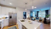 Located at 208 Windfall Way in Myrtle Beach, SC, this single-floor, 2-bedroom, 2-bathroom residence offers a thoughtfully planned open-concept layout that maximizes its efficient footprint. The kitchen serves as a central hub, showcasing white shaker cabinetry, sparkling quartz countertops, a large island with an undermount sink, stainless steel appliances, subway tile backsplash, and elegant glass pendant lighting. The space flows seamlessly into the dining area and living room, which features large windows with plantation shutters and floor-to-ceiling drapes, filling the space with natural light. The primary bedroom is a comfortable retreat featuring hardwood-style flooring, a ceiling fan, natural light from shuttered windows, and a bold accent wall. The second bedroom offers versatility, currently configured as a home office with a distinctive woven pendant light. Both bathrooms feature white vanities with quartz countertops. A dedicated laundry room with full-size washer and dryer adds convenience. Hardwood-style flooring runs throughout, tying together the clean, contemporary aesthetic of this well-appointed Myrtle Beach residence.
