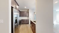 This single-floor residence on Whiskey Way in Ballston Spa, NY offers a thoughtfully designed layout with two bedrooms, one bathroom, and a combined kitchen and living area. Light-toned hardwood-style flooring runs throughout, creating a cohesive and clean aesthetic across all rooms.

The kitchen is a standout feature, showcasing rich dark-stained cabinetry with matte black hardware, light quartz countertops, and a classic white tile backsplash in a herringbone pattern. A large central island with an undermount sink and matte black faucet serves as both a functional workspace and a natural gathering point. Three pendant lights hang above the island, complementing the stainless steel appliances, including a French door refrigerator, electric range, and microwave.

The living area benefits from abundant natural light through multiple windows fitted with horizontal blinds, creating a bright and airy atmosphere. A glass-panel front door further enhances the light-filled entry.

Both bedrooms feature the same light flooring and neutral wall tones, with windows providing natural light. The primary bedroom offers a comfortable footprint with good proportions.

The bathroom includes a full tub-shower combination with white subway tile surround and matte black fixtures, maintaining the consistent modern design language found throughout the residence.