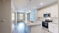 This well-appointed one-bedroom, one-bathroom residence in Suwanee, GA offers a thoughtfully designed open-concept layout with modern finishes throughout. Wood-look plank flooring runs continuously across the entire floor, creating a cohesive and contemporary aesthetic.

The kitchen serves as the centerpiece of the living area, showcasing a large granite-topped island with an undermount sink and pendant lighting overhead. Crisp white shaker cabinetry extends to the ceiling, providing generous storage, while stainless steel appliances — including a range, microwave, and refrigerator — complete the setup. The kitchen flows seamlessly into the living and dining area, which benefits from natural light and direct access to a private balcony through a glass-paneled door.

The spacious bedroom features a ceiling fan, a large window with outdoor views, and connects directly to the full bathroom. The bathroom is finished with granite countertops and a tiled tub-and-shower combination, with direct access to a dedicated walk-in closet equipped with built-in shelving — offering practical and organized storage.

Neutral tones, recessed lighting, and clean lines throughout give the space a bright, move-in-ready feel suited for comfortable everyday living in the Suwanee, GA area.