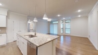 This well-appointed single-floor residence offers a thoughtfully designed open-concept layout that seamlessly connects the kitchen, dining, and living areas. The kitchen serves as the heart of the home, anchored by a generous granite-topped island with a built-in sink and pendant lighting overhead. White shaker-style cabinetry lines the walls, complemented by a classic subway tile backsplash, stainless steel appliances including a refrigerator, microwave, and range, and recessed lighting throughout. Warm hardwood-style flooring extends across the main living areas, enhancing the bright and airy ambiance. The living area is bathed in natural light from large sliding glass doors and dual windows, with crown molding adding an elegant architectural touch. The bedroom is spacious and carpeted, featuring multiple windows with abundant natural light and a ceiling fan. The bathrooms are finished to a high standard — one features a granite vanity and tiled tub surround with a glass block window, while the other showcases a walk-in glass-enclosed shower with marble-style subway tile walls, penny tile flooring, and a granite vanity. Together, these spaces create a cohesive, refined living environment with quality finishes at every turn.
