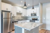This well-appointed one-bedroom, one-bathroom unit in Madison, WI, offers a thoughtfully designed open-concept layout with modern finishes throughout. The kitchen serves as a central highlight, featuring crisp white shaker cabinetry with matte black hardware, striking granite countertops, a central island with stylish pendant lighting, and a full suite of stainless steel appliances including a refrigerator, range, microwave, and dishwasher. Light hardwood-style flooring flows seamlessly through the main living areas, creating a cohesive and airy atmosphere. The living room is bright and inviting, with a sliding glass door that opens to a private balcony offering pleasant outdoor views of the surrounding greenery. The bedroom is carpeted for comfort, fitted with a ceiling fan, and features a large window that brings in natural light. A spacious walk-in closet with wire shelving provides ample storage. The bathroom is finished with a granite-topped white vanity, a modern wall sconce, and a rectangular mirror, maintaining the unit's clean, contemporary aesthetic. A dedicated closet with in-unit laundry hookups adds everyday convenience, completing this efficiently designed and move-in-ready space.