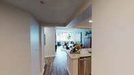 This thoughtfully designed single-floor residence offers a cohesive and contemporary living experience. The open-concept layout connects the kitchen and living area seamlessly, with wood-look flooring running throughout to unify the space. 

The living room is bathed in natural light from large windows that frame urban views of the surrounding cityscape. Soft blue-toned walls create a calm, inviting atmosphere, complemented by clean white trim and recessed lighting overhead.

The kitchen is outfitted with stainless steel appliances, including a range and over-the-range microwave, set against white shaker-style cabinetry with modern hardware. A light blue subway tile backsplash adds a subtle pop of color, while granite countertops provide ample workspace. A breakfast bar opens directly to the living area, enhancing the open flow.

The primary bedroom features a large window with urban views, neutral walls, and a built-in closet with shelving and hanging storage. The second bedroom offers its own oversized window and a serene blue accent wall, providing a restful retreat.

Together, the rooms reflect a consistent design language — light, airy, and modern — making this a well-balanced and functional living space.