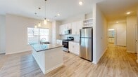Located at 5895 Arbor Isle Way in Myrtle Beach, South Carolina, this single-story home offers a clean, modern design throughout. Light wood-look flooring runs through the main living and wet areas, while plush carpet adds comfort to the bedrooms and living room.

The kitchen is a standout feature, showcasing white shaker cabinetry, granite countertops, a center island with a built-in sink, stainless steel appliances including a refrigerator, range, and microwave, plus a built-in wine rack. Large windows flood the kitchen with natural light, creating a bright and welcoming atmosphere.

The living room is generously sized with a ceiling fan, wide windows, and glass double doors that open to an outdoor area, allowing ample natural light and outdoor views. The layout flows seamlessly from the kitchen into the living space.

The bedrooms are carpeted and well-proportioned, each with ceiling fans and windows that bring in natural light. The primary suite connects to a private en-suite bathroom featuring a granite vanity, glass-enclosed walk-in shower, and a spacious walk-in closet with wire shelving. A second bathroom offers a full soaking tub and shower combination with built-in shelving. A light-filled hallway connects the rooms, completing this well-appointed single-level home.