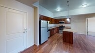 Located at 932 Cypress Rd in Saint Cloud, Minnesota, this single-floor unit offers a well-designed, open-concept layout that seamlessly connects the kitchen, dining, and living areas. The kitchen is a standout feature, showcasing rich dark wood cabinetry extending to the ceiling, granite-style countertops, stainless steel appliances including a range, microwave, refrigerator, and dishwasher, and a center island with pendant lighting overhead. Warm hardwood flooring runs throughout the kitchen and main living space, transitioning to plush carpet in the living and bedroom areas. The living room features vaulted ceilings that lend an airy, open feel, with natural light entering through windows that offer views of the surrounding neighborhood. The bedrooms are comfortably sized with carpet flooring, windows for natural light, baseboard heating, and wall-mounted air conditioning units. The bathrooms are finished with tile flooring, wood vanities, white countertops, large mirrors, and accessible grab bars in the full bath, which also includes a tub and shower combination. Overall, the space presents a functional and comfortable layout with consistent, quality finishes throughout.