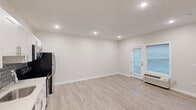 Located at 1528 W Girard Ave in Philadelphia's vibrant Brewerytown neighborhood, this one-bedroom, one-bathroom unit offers a well-designed and efficiently utilized floor plan. The open living area flows naturally from the kitchen, featuring light wood-style flooring, recessed lighting, and crisp white walls throughout, creating a bright and clean aesthetic. A glass-paned door leads to a private outdoor patio area, adding a welcome extension of the living space.

The kitchen is thoughtfully appointed with white shaker-style cabinetry, a gray subway tile backsplash, white quartz countertops, and a full suite of stainless steel appliances including a refrigerator, electric range, over-the-range microwave, and dishwasher. The layout maximizes functionality without sacrificing style.

The bedroom is carpeted for comfort and includes a ceiling fan with light fixture, a wall-unit HVAC system, and a window that allows natural light to filter in. The bathroom features tile flooring, a walk-in tiled shower, a rich wood vanity with a white countertop and undermount sink, and a framed mirror. A utility room completes the unit. The building itself is a multi-story structure with a compact outdoor courtyard area.