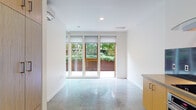 This thoughtfully designed single-floor space embodies a clean, contemporary aesthetic throughout. Polished concrete floors extend seamlessly from room to room, lending an industrial-modern character that ties the entire layout together.

The open-plan kitchen is a standout feature, outfitted with warm bamboo cabinetry, concrete countertops, and a bold dark metal backsplash. Stainless steel appliances — including a gas cooktop, wall oven, dishwasher, and a statement overhead range hood — provide a professional-grade cooking experience. Open shelving adds both functionality and visual interest to the space.

The living area is bathed in natural light, courtesy of a full-width wall of floor-to-ceiling glass sliding doors that open directly onto a private outdoor patio surrounded by lush greenery. This seamless indoor-outdoor connection creates an airy, expansive feel. A wall-mounted mini-split system ensures year-round climate comfort.

The bathroom is finished with clean white subway tile in the tub surround, a bamboo vanity with an integrated sink, and consistent concrete flooring that echoes the rest of the home.

A dedicated laundry area houses a full-size side-by-side washer and dryer with built-in shelving above, adding practical convenience. Crisp white walls and recessed lighting throughout complete the space's refined, minimalist character.