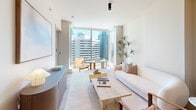 Located in the heart of Seattle's Belltown neighborhood, this thoughtfully designed one-bedroom, one-bathroom residence offers an efficient yet refined living experience across a single floor. The open-plan living, dining, and kitchen area serves as the centerpiece of the home, where light wood flooring, neutral tones, and clean lines create a cohesive modern aesthetic. Floor-to-ceiling windows in the living room flood the space with natural light while framing striking views of the Seattle skyline, making the area feel open and airy despite its compact footprint.

The kitchen is outfitted with flat-front cabinetry in a soft grey finish, an integrated cooktop, under-cabinet lighting, and a central island that doubles as additional prep space and casual dining. Built-in open shelving adds both storage and character. A dedicated dining area with pendant lighting sits adjacent to the kitchen, completing the social hub of the home.

The bedroom features large windows with city views, providing ample natural light, and includes closet space for practical storage. The bathroom is finished with elegant marble-style tile surrounding a soaking tub, accented by matte black fixtures for a contemporary touch. A dedicated laundry area adds everyday convenience to this polished urban residence.