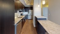 This thoughtfully designed single-floor residence combines contemporary style with functional living across an open, flowing layout. The living area is anchored by stunning floor-to-ceiling windows that flood the space with natural light and frame sweeping city and treetop views, complemented by smooth hardwood flooring that extends throughout the main areas. A set of sliding glass doors opens to a private balcony, further enhancing the connection to the outdoors.

The gourmet kitchen is a standout feature, outfitted with rich dark espresso cabinetry, granite countertops, a full suite of stainless steel appliances, a subway tile backsplash, and warm hardwood floors. Pendant lighting and recessed track lighting add a polished, modern touch, while a generous island with matching granite provides additional prep and dining space.

The bedroom offers a calm retreat with plush carpeting, neutral tones, and direct access to the outdoors through a sliding glass door, offering tranquil views of the surrounding greenery and skyline. The full bathroom is clean and contemporary, featuring large-format tile flooring, a tub and shower combination with white tile surround, granite vanity countertop, and dark cabinetry that ties seamlessly to the kitchen's aesthetic. Throughout the residence, a cohesive neutral palette and quality finishes create an inviting and refined atmosphere.