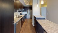 This thoughtfully designed single-floor residence combines contemporary style with functional living across an open, flowing layout. The living area is anchored by stunning floor-to-ceiling windows that flood the space with natural light and frame sweeping city and treetop views, complemented by smooth hardwood flooring that extends throughout the main areas. A set of sliding glass doors opens to a private balcony, further enhancing the connection to the outdoors.

The gourmet kitchen is a standout feature, outfitted with rich dark espresso cabinetry, granite countertops, a full suite of stainless steel appliances, a subway tile backsplash, and warm hardwood floors. Pendant lighting and recessed track lighting add a polished, modern touch, while a generous island with matching granite provides additional prep and dining space.

The bedroom offers a calm retreat with plush carpeting, neutral tones, and direct access to the outdoors through a sliding glass door, offering tranquil views of the surrounding greenery and skyline. The full bathroom is clean and contemporary, featuring large-format tile flooring, a tub and shower combination with white tile surround, granite vanity countertop, and dark cabinetry that ties seamlessly to the kitchen's aesthetic. Throughout the residence, a cohesive neutral palette and quality finishes create an inviting and refined atmosphere.