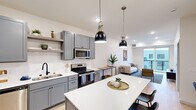 This single-floor residence offers a thoughtfully designed open-concept layout that seamlessly connects the kitchen, dining, and living areas. The kitchen is a standout feature, showcasing gray shaker-style cabinetry, white quartz countertops, a subway tile backsplash, and a full suite of stainless steel appliances including a refrigerator, range, microwave, and dishwasher. A central island with seating provides additional prep and dining space, while two black industrial-style pendant lights add a stylish focal point overhead. Open shelving offers practical storage and display space. The living area is bright and welcoming, with light hardwood flooring, recessed lighting, and a large sliding glass door that opens to a private balcony with outdoor views. The space flows naturally into two well-proportioned bedrooms, each carpeted for comfort. One bedroom features direct access to the full bathroom, while a window allows natural light to fill the room. The bathroom is finished with gray vanity cabinetry, white countertops, light wood-look flooring, and matte black fixtures throughout, complemented by a tub-shower combination. Clean white walls, consistent modern hardware, and an airy, neutral palette give the entire residence a cohesive, contemporary feel.