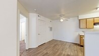 This single-story residential unit offers a practical and well-organized layout designed for comfortable everyday living. The heart of the home is an open-concept kitchen and living area, where warm-toned wood-look flooring extends throughout, creating a cohesive and inviting atmosphere. The kitchen features light oak cabinetry with ample storage, a white countertop peninsula with a built-in sink, and black appliances including a range and refrigerator, all beneath a textured ceiling. The living area is bright and open, benefiting from natural light streaming through a window fitted with white blinds, and includes a ceiling fan for added comfort. A dedicated dining or flex space adjacent to the kitchen also features a ceiling fan and continues the wood-look flooring. The bedrooms are carpeted for warmth and comfort, each offering generous proportions. The primary bedroom includes a wide sliding-door closet, a ceiling fan, and a window that allows natural light. Additional rooms provide versatile spaces suitable for various needs. The bathroom is clean and functional, featuring a full-size soaking tub with a shower surround. Throughout the unit, white six-panel doors, neutral white walls, and consistent finishes contribute to a clean, move-in-ready aesthetic.