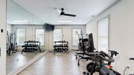 Located at 1001 Riverland Woods Pl in Charleston, SC, this fitness center offers a thoughtfully designed, single-floor workout facility that balances functionality with a clean, modern aesthetic. The space is organized into distinct activity zones, all unified by light wood-look flooring and crisp white walls that contribute to a bright, energizing atmosphere.

Upon entry, guests are welcomed by a striking living green wall featuring a motivational sign — a bold decorative statement that sets an encouraging tone. The cardio zone houses multiple treadmills and stationary cycling bikes, equipped with individual screens and positioned near windows that allow natural light to filter in. Ceiling fans overhead promote airflow throughout the space.

The strength training area features a comprehensive dumbbell rack alongside multi-use cable and weight machines, with floor-to-ceiling mirrors along one wall to maximize the sense of space and support proper form. A dedicated open-floor stretching and flexibility zone includes a massage chair, resistance bands, and yoga accessories, separated from the main floor by a sheer curtain partition for a more relaxed environment.

Throughout the facility, large windows with white blinds provide views of the surrounding greenery, reinforcing the connection to the natural Charleston landscape. The overall design is clean, well-lit, and purposefully equipped to support a full range of fitness activities.
