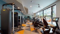 Located at 2869 NE Sandy Blvd in Portland, Oregon, this fitness center is a thoughtfully designed, single-floor facility offering a comprehensive workout environment. The space is characterized by its eye-catching geometric-patterned flooring in bold orange, gray, and beige tones, which adds a dynamic and energetic aesthetic throughout.

Large floor-to-ceiling windows line the perimeter, flooding the interior with abundant natural light and providing views of the surrounding neighborhood. Ceiling fans are distributed across the length of the space, ensuring comfortable airflow during workouts.

The main fitness floor is generously proportioned and lined with full-length mirrors that enhance the sense of openness. It is well-stocked with a wide array of cardio equipment, including treadmills, elliptical trainers, and stationary bikes, as well as a robust selection of strength-training machines. A dedicated free weights area features dumbbells, benches, resistance tools, and stability balls, catering to a variety of training styles.

A glass-enclosed studio area is set apart from the main floor, housing cycling bikes and offering a focused space for group or individual cycling sessions. Accent walls in deep teal add a bold design element, complemented by curated artwork that contributes to the motivating atmosphere. The overall ambiance is modern, bright, and well-organized, making this fitness center a fully functional and visually engaging facility.