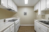 Located at 175 North Feldner Road in Orange, California, this thoughtfully laid-out single-floor unit makes excellent use of its compact footprint. The open-concept kitchen and living area serves as the heart of the space, creating a seamless flow between cooking and relaxing. The kitchen is well-equipped with white cabinetry — both upper and lower — offering ample storage, complemented by speckled laminate countertops, a gas range, a stainless steel sink, and a ventilation hood. A skylight-style overhead light fixture brightens the kitchen, while a window provides a view into the living area, enhancing the sense of openness. The living area features warm light wood laminate flooring that extends throughout the unit, neutral beige walls, and clean white trim. A wall-mounted heating unit provides climate control, and a mirrored sliding-door closet offers practical storage. A hallway connects the main living space to the full bathroom, which includes a tub-shower combination with a curtain rod, a toilet, and a clean, all-white finish. The overall aesthetic is bright, clean, and functional — an efficiently designed space ideal for comfortable everyday living in the heart of Orange, CA.