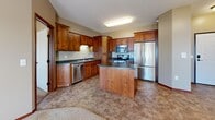 Located at 555 Victory Ave S in Sartell, Minnesota, this single-floor, 2-bedroom, 2-bathroom unit offers a practical and comfortable layout. The kitchen is a standout feature, showcasing warm-toned wood cabinetry, dark countertops, a central island, and a full suite of stainless steel appliances including a refrigerator, range, microwave, and dishwasher — all set on durable tile-style flooring. The open living area flows naturally from the kitchen and is finished with plush carpeting, baseboard heating, and a large window that brings in natural light and outdoor views of the surrounding landscape. Both bedrooms are carpeted and generously sized, each equipped with baseboard heaters and windows that invite natural light. The primary bedroom includes direct access to an en-suite bathroom featuring a wood vanity, white countertop, and tile flooring. A second full bathroom offers a tub-shower combo, wood vanity, and matching tile floors. Two closets provide ample storage, with at least one featuring built-in wire shelving. Warm-toned walls, rich wood trim, and consistent finishes throughout contribute to a cohesive and inviting ambiance across the entire unit.