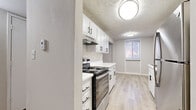 Located at 1012 Emery Rd in Lawrence, Kansas, this single-floor residence offers two bedrooms and two full bathrooms in a thoughtfully laid-out floor plan. The combined kitchen and living room area serves as the heart of the home, featuring light wood-style luxury vinyl flooring that creates a clean, cohesive aesthetic. The galley-style kitchen is well-appointed with crisp white cabinetry with black hardware, light-toned countertops, stainless steel appliances including a range and refrigerator, and a stainless steel sink — all complemented by a textured ceiling and flush-mount lighting. The open living area flows naturally from the kitchen, offering a bright, neutral canvas with ample room to arrange furnishings. Both bedrooms are finished with plush carpet and feature neutral walls that lend a calm, comfortable atmosphere. The spacious primary bedroom includes direct access to a full bathroom and a dedicated closet. A secondary bedroom benefits from a large window that invites natural light. A well-organized hallway closet provides additional built-in shelving for storage needs. The bathrooms are clean and functional, each featuring a full tub-shower combination. Two hallways connect the rooms efficiently, rounding out this practical and move-in-ready home.