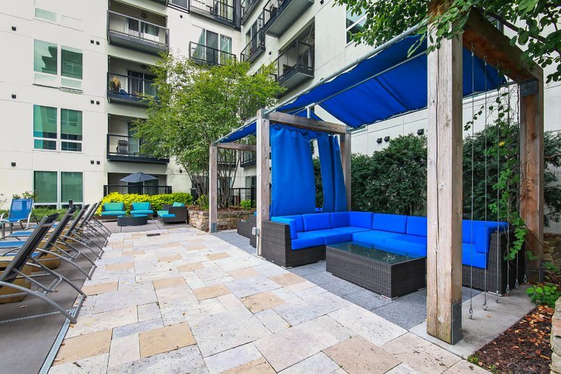 Outdoor lounge area with blue sectional sofa and cabana overlooking apartment building.