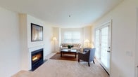 This single-floor residence offers a thoughtfully designed layout that balances comfort and functionality throughout. The living room serves as the centerpiece of the home, featuring a classic fireplace framed by a clean white mantle, soft wall-to-wall carpeting, and French doors that welcome an abundance of natural light. Multiple windows fitted with blinds further brighten the space, creating a warm and inviting atmosphere. The kitchen is outfitted with stainless steel appliances—including a refrigerator, gas range, and microwave—complemented by light wood cabinetry, granite-style countertops, and hardwood flooring, providing a practical yet stylish cooking environment. The primary bedroom is generously sized and features a charming built-in window seat, plush carpeting, and ample room for a full dresser and additional furnishings. The second bedroom is equally comfortable, with carpeted floors, a window for natural light, and convenient access to closet storage. Both bathrooms are finished with hardwood-style flooring, wood-framed vanity mirrors, granite-style countertops, light wood cabinetry, and tub-shower combinations. Throughout the home, a neutral color palette and consistent finishes contribute to a cohesive, serene ambiance.